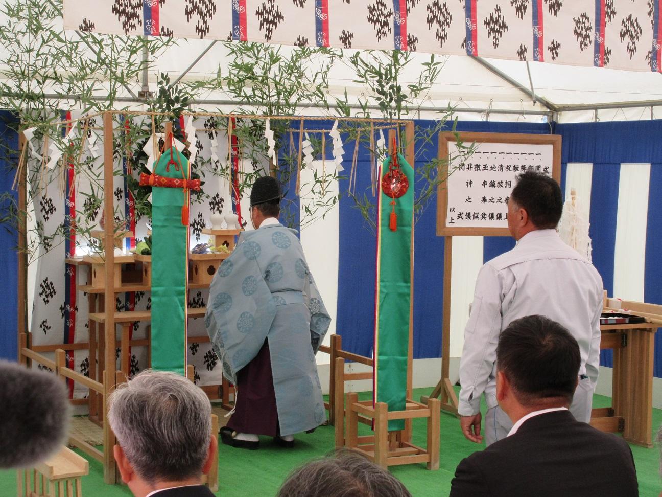神職が安全祈願をしている様子を座って見ている関係者と、神職の後ろの立つ男性の写真