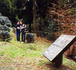 山中で後方には木々が生い茂った開けた場所に案内表示版が設置されており、女性二人が表示版の方を見ている写真